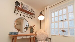 A cozy room with a wooden desk, a chair with a fluffy cushion, a round mirror, and a window with a view of the outside. - Little Gem (Whitby)