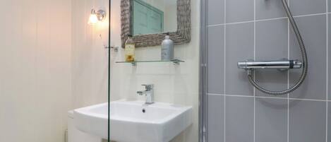 Et badeværelse med en glasafskærmet brusekabine, en hvid vask og et toilet.