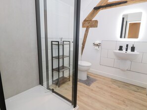 A modern bathroom with a glass shower enclosure, a white toilet, and a wooden beam ceiling. - Y Stabl (Corwen)
