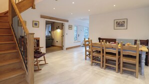 A spacious room with a wooden staircase, a dining area with wooden chairs and a table, and a cozy seating area with a rocking chair. - Y Stabl (Corwen)