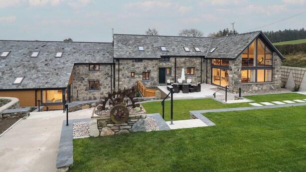 A stone house with a patio, outdoor seating, and a large window. - Y Stabl (Corwen)