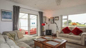 Ein Wohnzimmer mit einer Couch, einem Couchtisch und einem Kamin. Ein großes Fenster mit Vorhängen und ein Gemälde an der Wand.