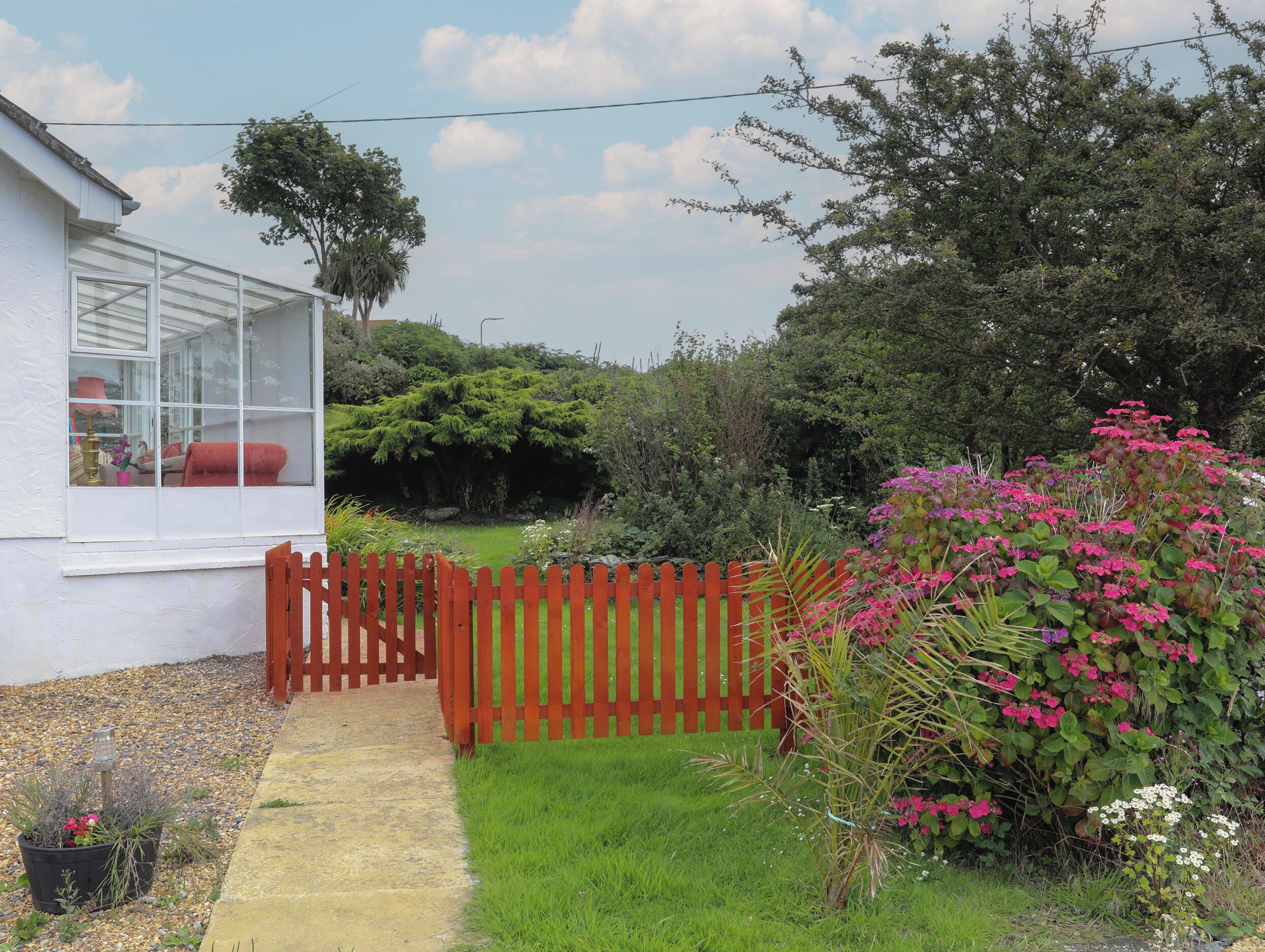 A house with a glass door, a wooden fence, and a garden with various plants and flowers.