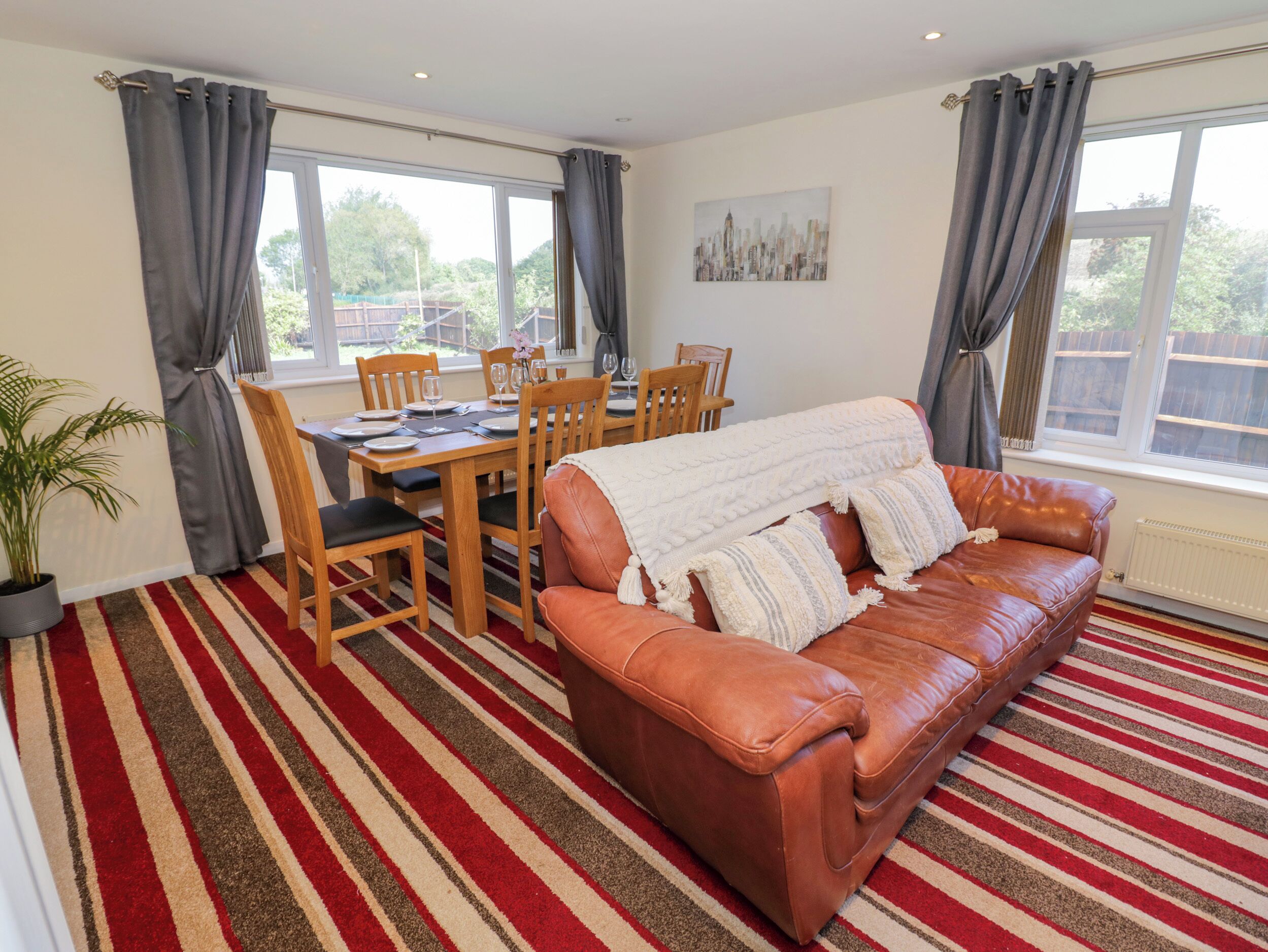 A living room with a brown leather sofa, a dining table with chairs, and a striped carpet.