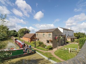 A riverside building with a docked boat, a grassy area, and a wooden fence. - Fenny Marina Cottage (Southam)