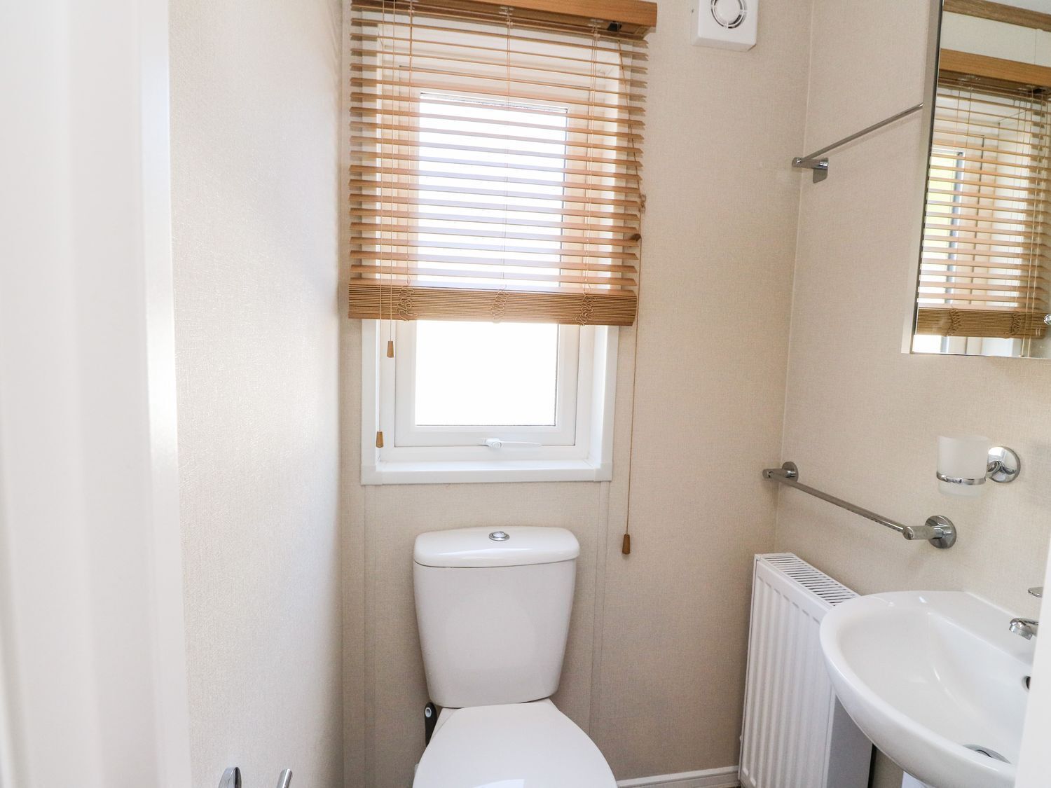 Ein kleines Badezimmer mit Toilette, einem Fenster mit Jalousien, einem Heizkörper und einem Waschbecken.