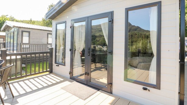 En moderne mobilhome med terrasse, store skydedøre og udsigt til et bjerglandskab.
