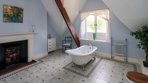 A bathroom with a freestanding bathtub, a window with curtains, a radiator, and a peacock-themed painting on the wall. - North Wing (Belford)