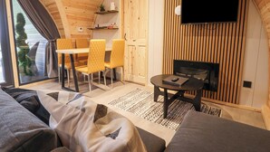 Un intérieur chaleureux avec un plafond en bois aux lignes courbes, un coin repas avec des chaises jaunes, un téléviseur à écran plat et un canapé.