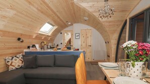 Un intérieur chaleureux et rustique, avec un canapé, une table à manger et des chaises. On aperçoit un coin cuisine au fond.