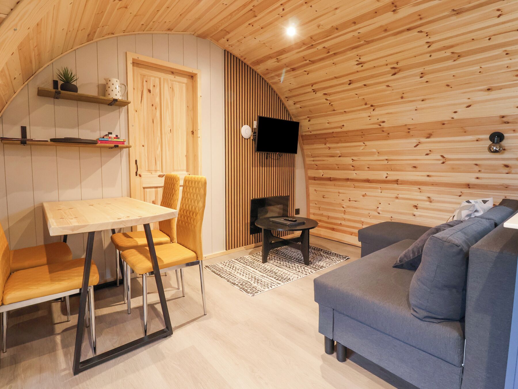 A cozy room with a wooden ceiling, a dining table with chairs, a sofa, and a television mounted on the wall.