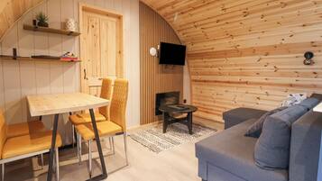 A cozy room with a wooden ceiling, a dining table with chairs, a sofa, and a television mounted on the wall.