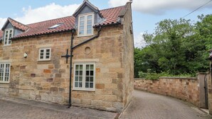 A stone building with a red-tiled roof, two windows, and a brick pathway leading to it. - Clematis Cottage (Whitby)