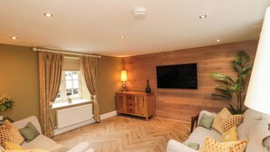 A living room with a herringbone floor, two sofas with patterned cushions, a wooden cabinet, a floor lamp, and a large plant. - Clematis Cottage (Whitby)