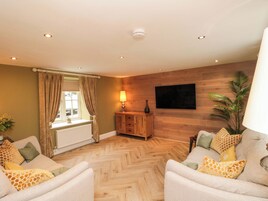 Un salón con suelo de espiga, dos sofás con cojines estampados, un mueble de madera, una lámpara de pie y una planta grande.