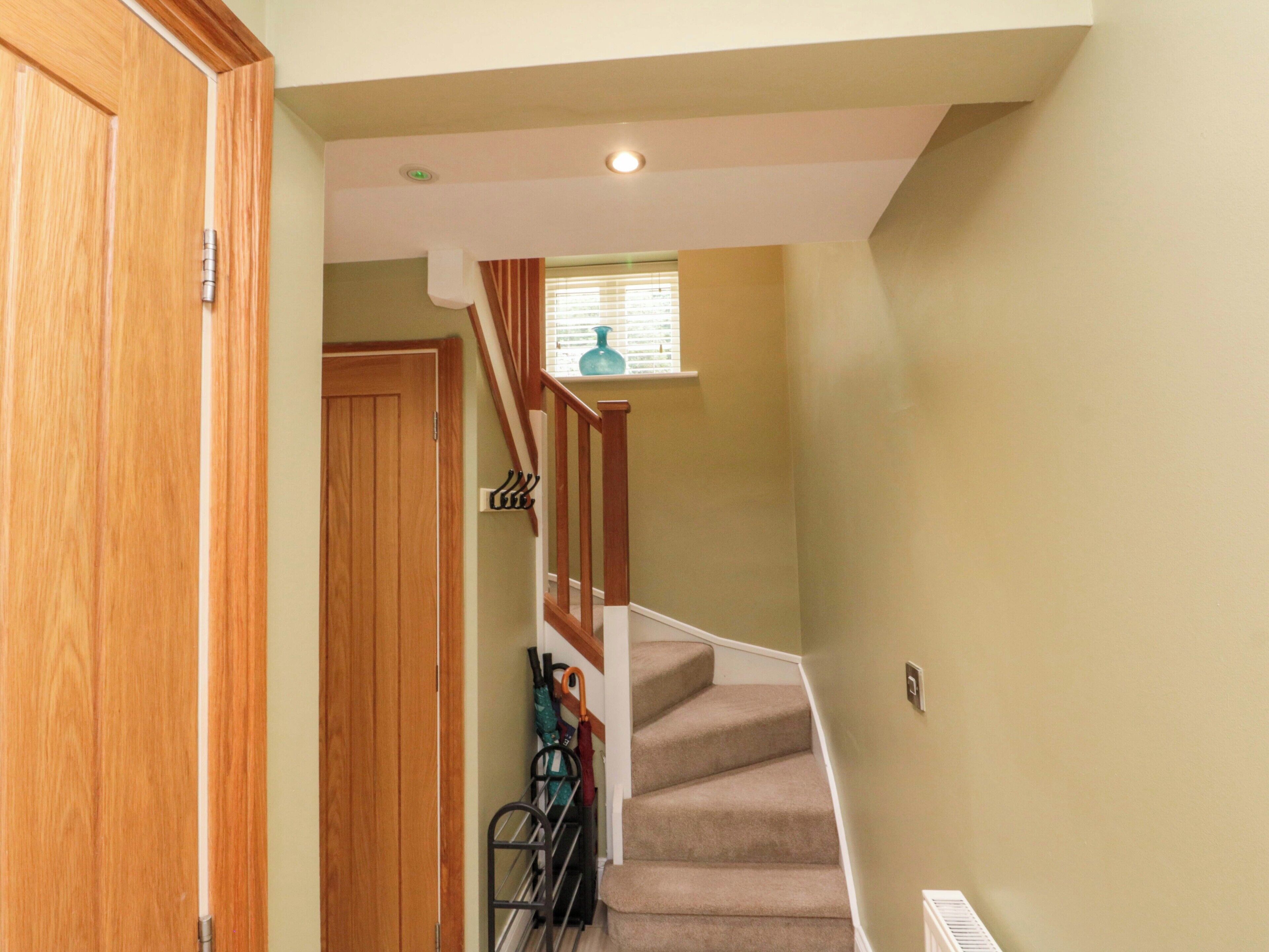 A staircase with a wooden handrail and beige carpet, leading to a room with a window and a door.