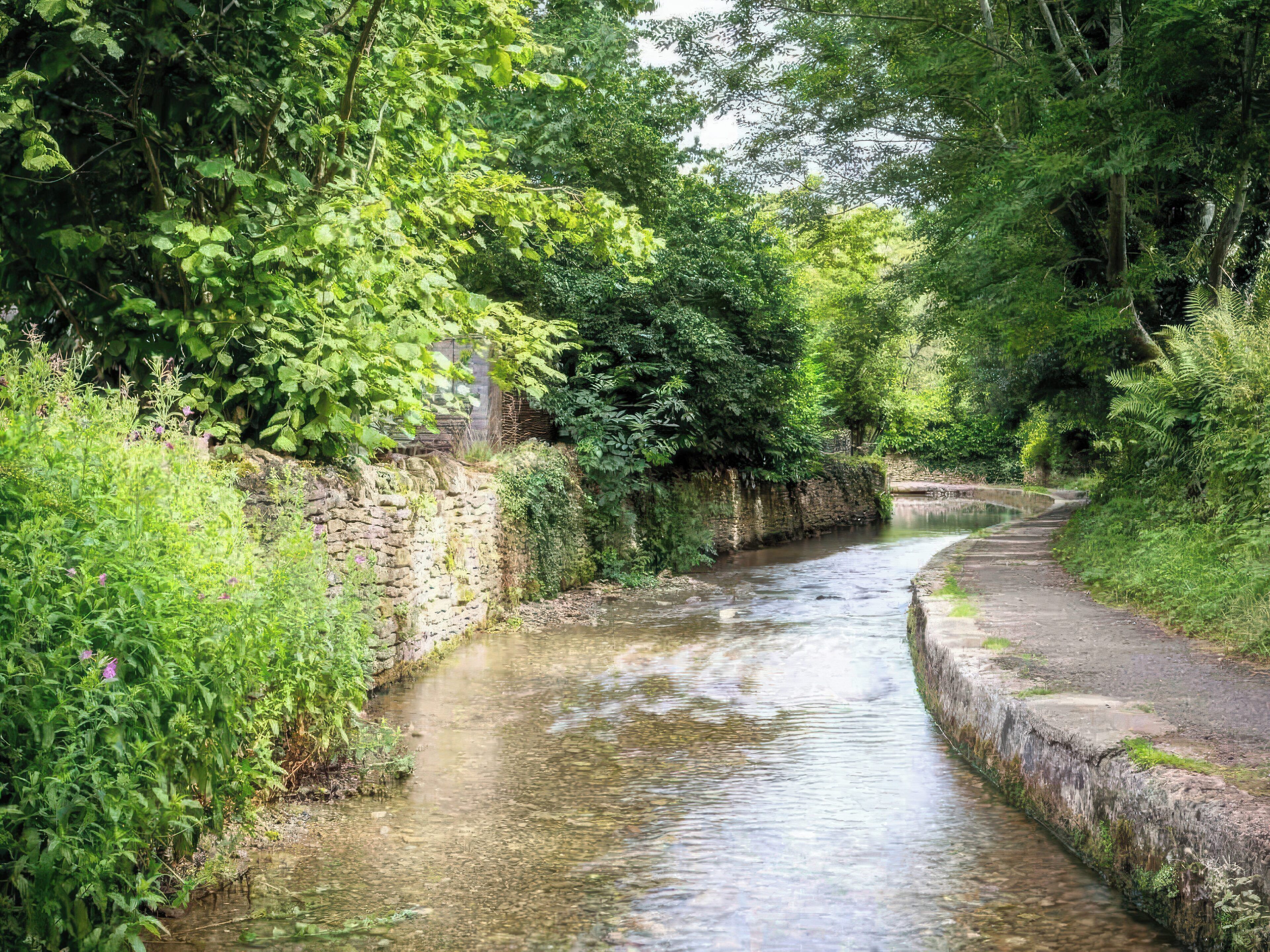 A narrow waterway flanked by lush greenery and stone walls.