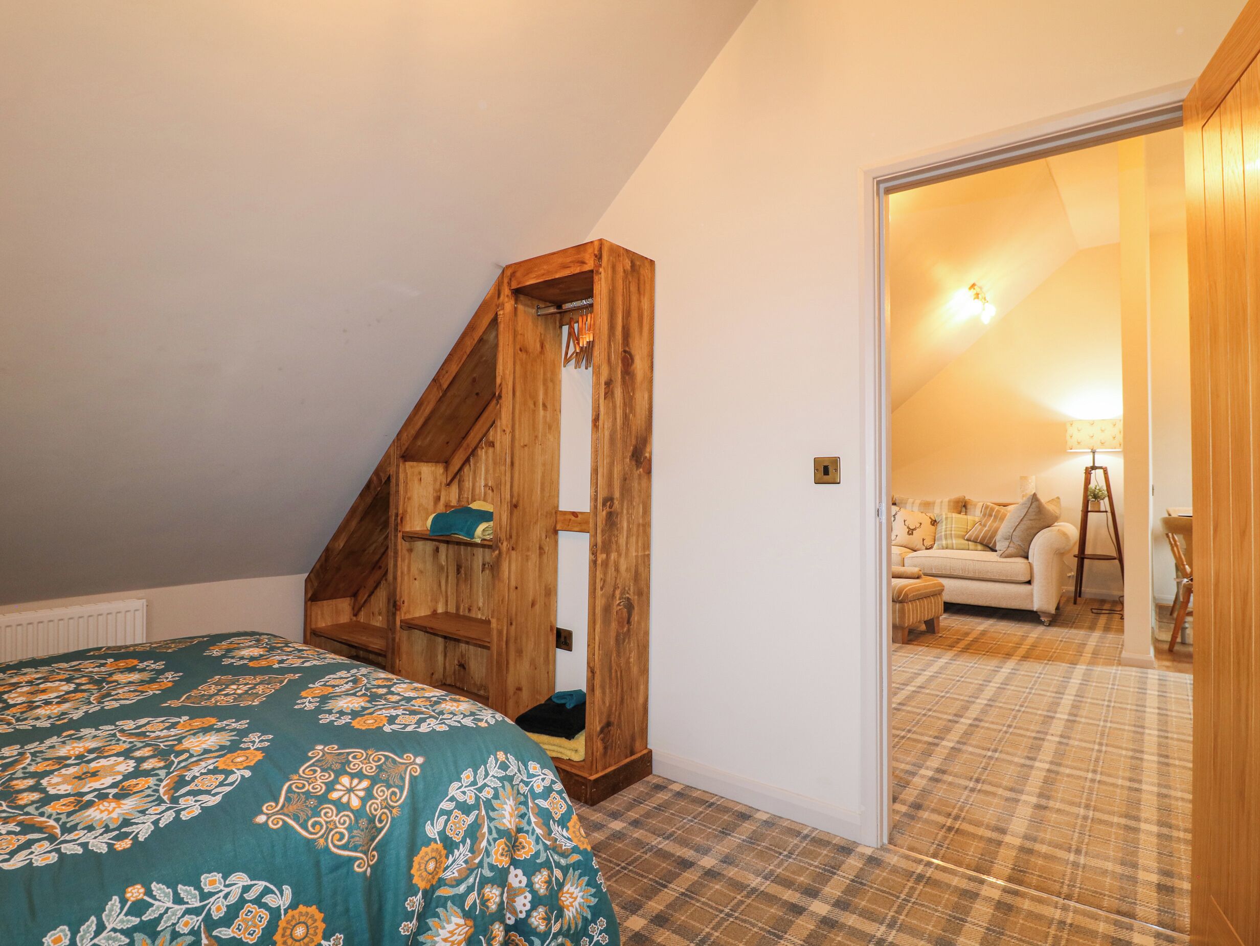 Une chambre avec un plafond en pente, un lit mezzanine en bois, un tapis à carreaux et un coin salon confortable avec une lampe et des coussins.