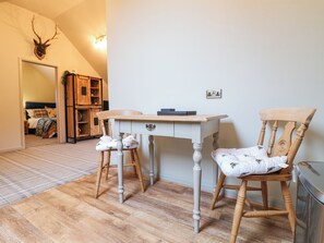 A room with a wooden desk, two chairs, a bed, and a wall-mounted deer head.
