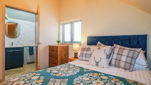 A bedroom with a bed, a dresser, a nightstand, a window, and a bathroom visible through an open door. - The Oak Room - Windmill Country Retreats (Melton Mowbray)