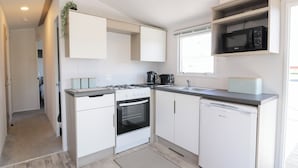 Cocina compacta con armarios blancos, estufa a gas, microondas y lavavajillas.