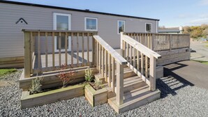 Una casa móvil con terraza de madera y rampa de acceso a la entrada.