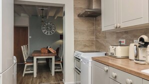 Een kleine keuken met witte kastjes, een houten aanrecht, een fornuis, een broodrooster en een klok aan de muur.
