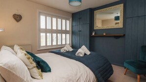 Een slaapkamer met een bed, een raam met blinds, een spiegel en een blauwgroene hanglamp.