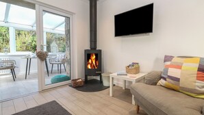 A cozy living room with a fireplace, a sofa, a TV, and a dining area with chairs and a table. - The Duck House (Penzance)
