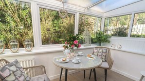 A conservatory with wicker furniture, a round table, and a view of lush greenery. - The Duck House (Penzance)