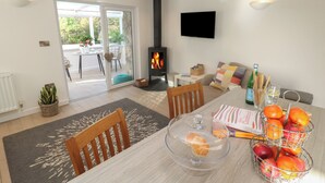 A cozy living room with a fireplace, a dining area with a table set for two, and a comfortable seating area with a sofa. - The Duck House (Penzance)