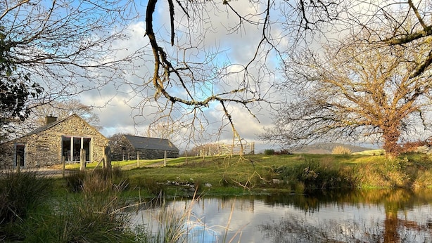 Ein Steinhaus mit einem großen Fenster und einer Tür, umgeben von einer Rasenfläche und einem Teich.