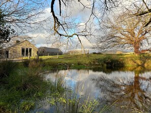 A stone building with a large window and a door, surrounded by a grassy area and a pond. - Hafod Y Llyn (Porthmadog)