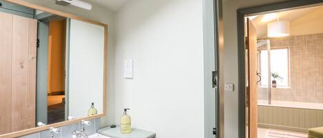Un baño con un lavamanos blanco, dos grifos, un espejo y una lámpara sobre el espejo.