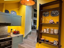 Una cocina con una pared amarilla, una repisa de madera con platos y una estufa roja.