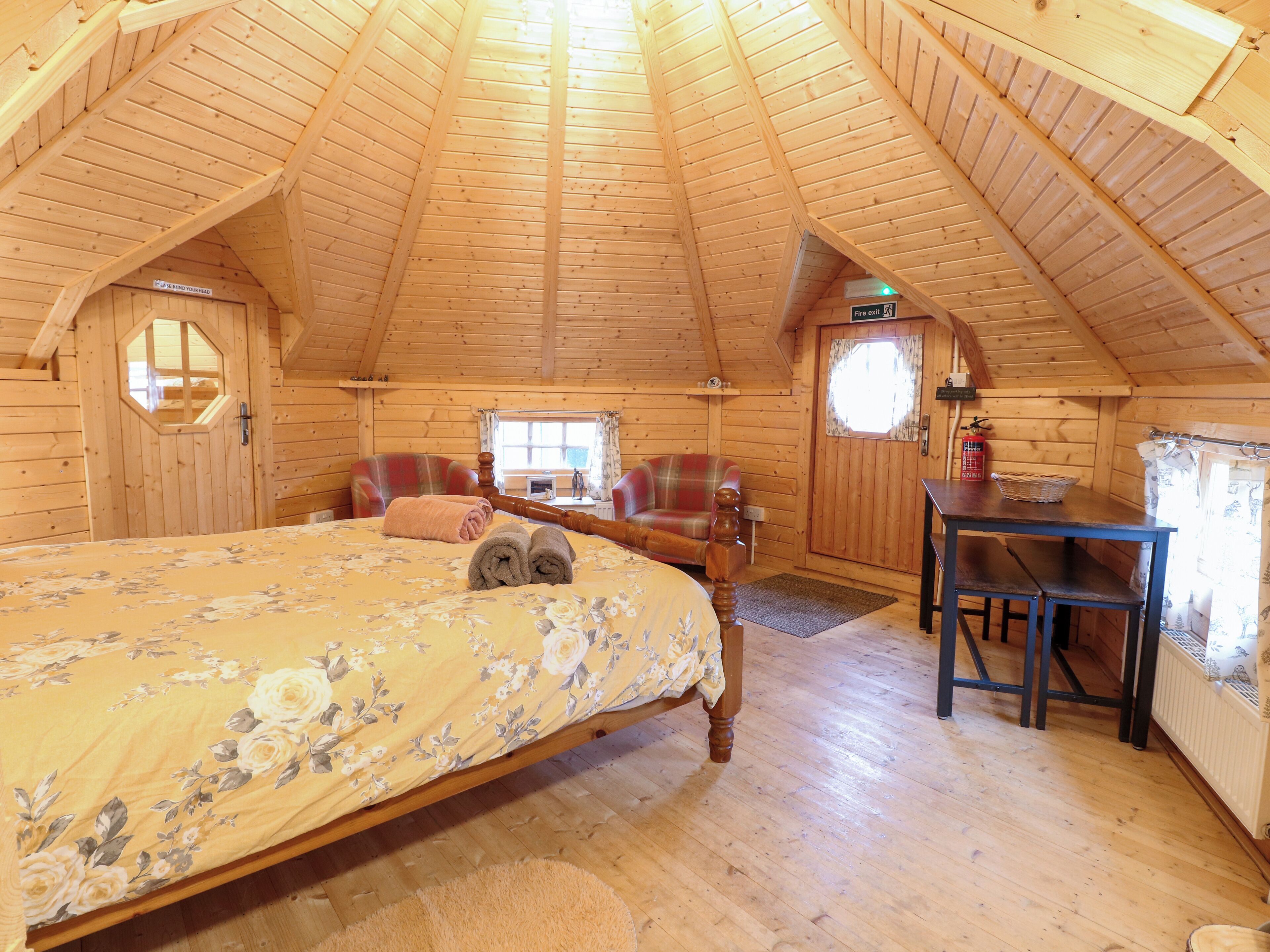 Une chambre confortable dans un chalet en rondins, avec un lit, deux fauteuils, une table et une cheminée.