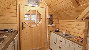 A wooden cabin interior with a kitchen area, a wooden door with a window, and a sign above the door. - Enchanted Cottage (King's Lynn)
