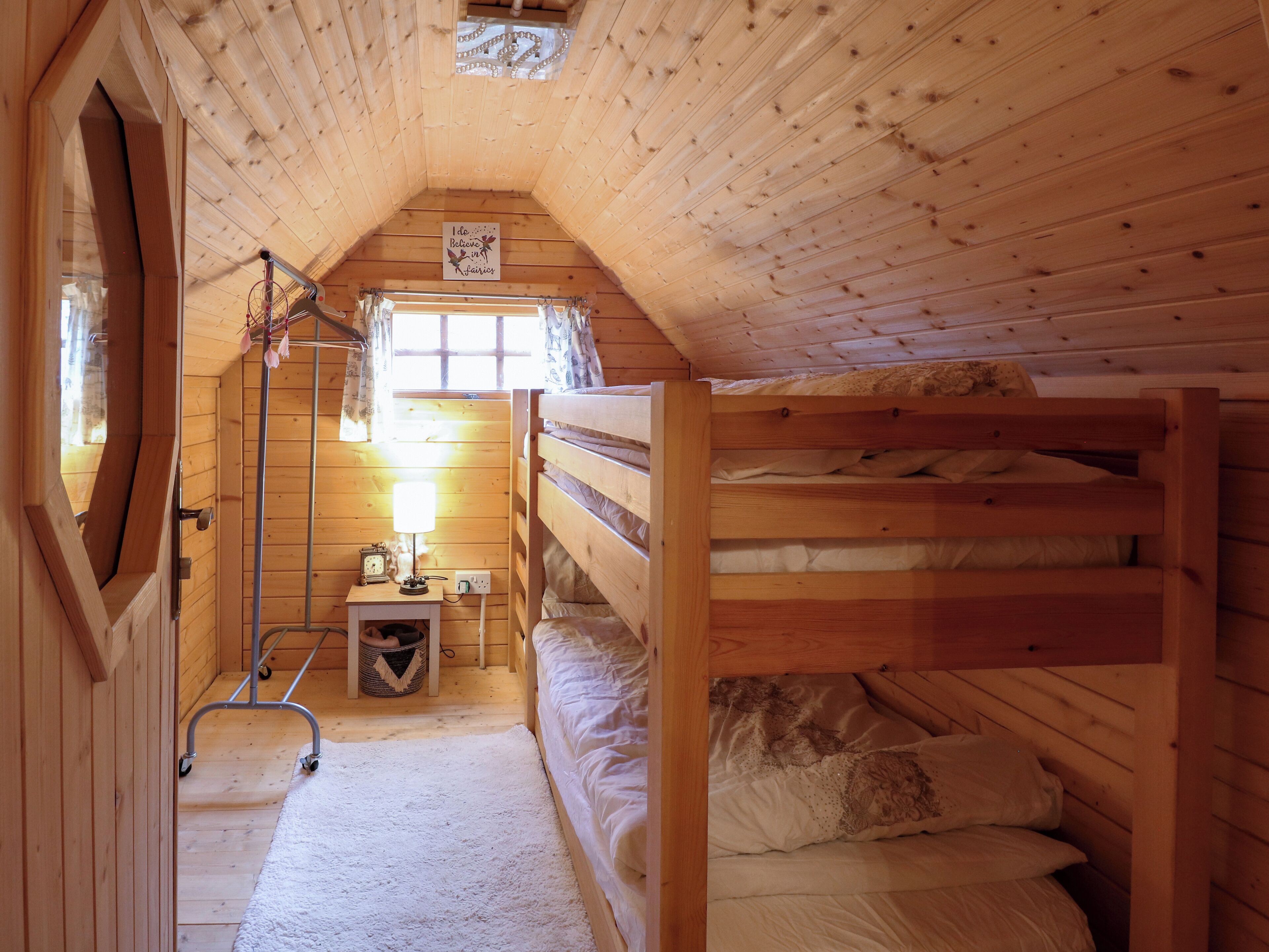 Ein gemütliches Holzhütten-Zimmer mit Etagenbetten, einem kleinen Tisch mit Lampe und einem Fenster mit Vorhängen.