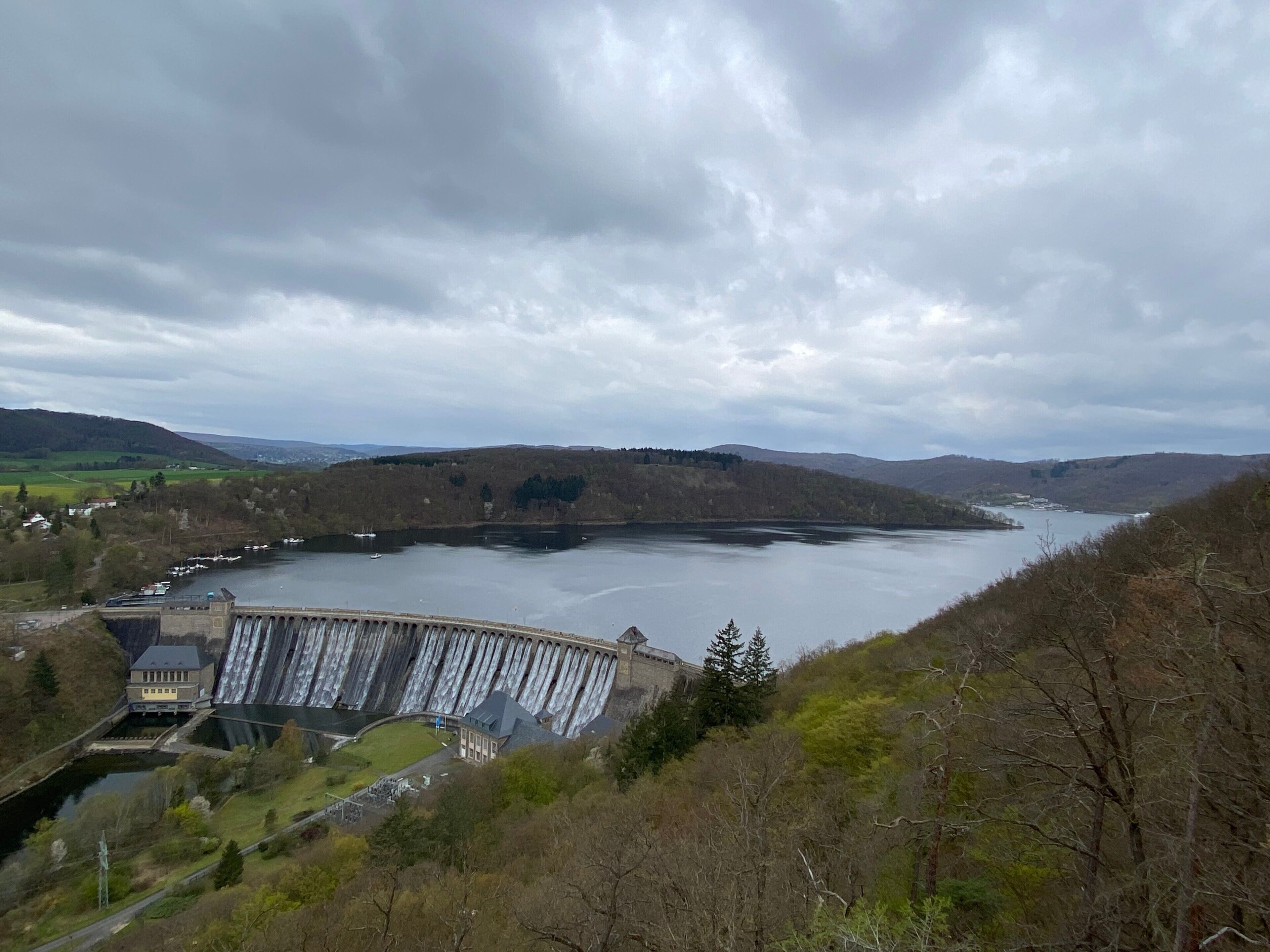 A large dam with a water reservoir, a bridge, and surrounding hills.
