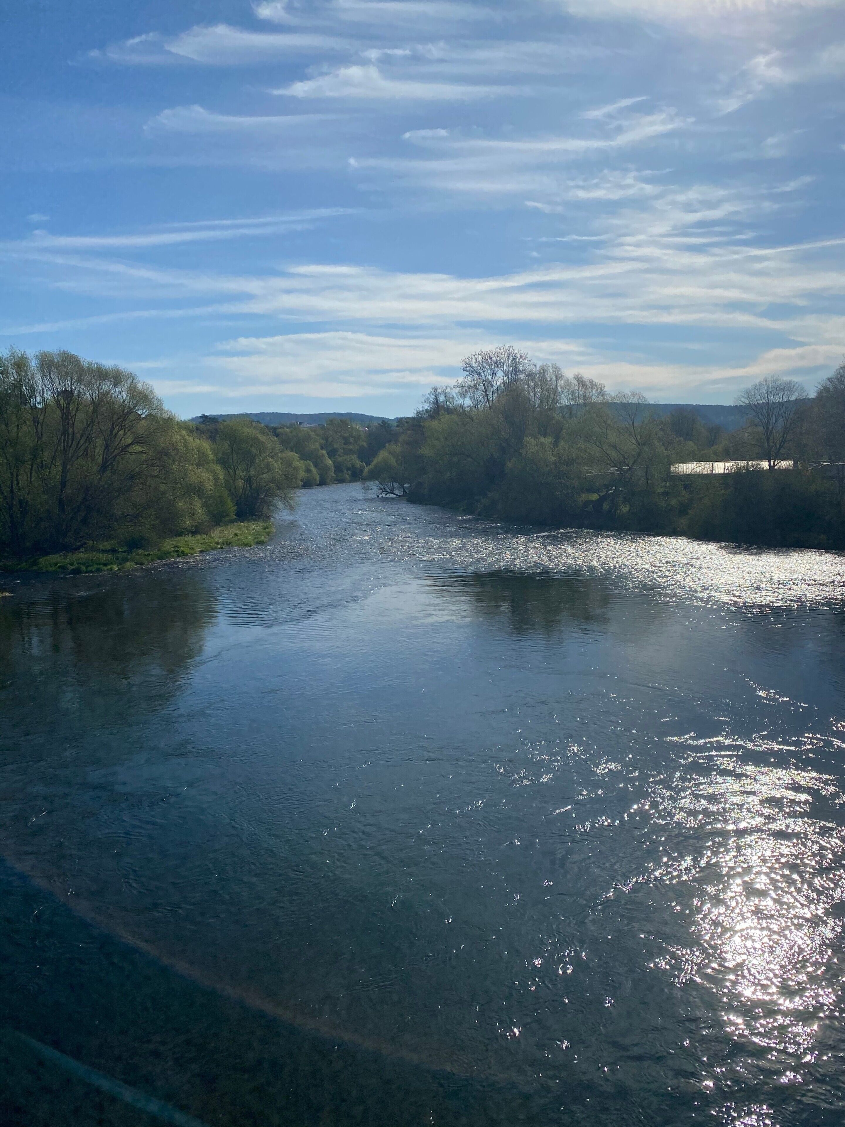 A river with trees on both sides, a clear sky, and distant hills.