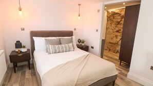 Ein Schlafzimmer mit einem großen Bett, zwei Nachttischen, einer Wandleuchte und einer strukturierten Wandverkleidung.