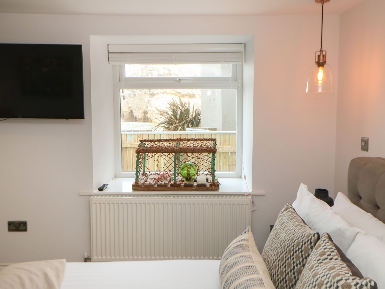 Un dormitorio con ventana, radiador, televisor, sofá y lámpara colgante.