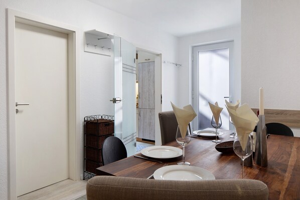 A dining area with a wooden table set for two, chairs, a vase with a candle, and a mirror on the wall.