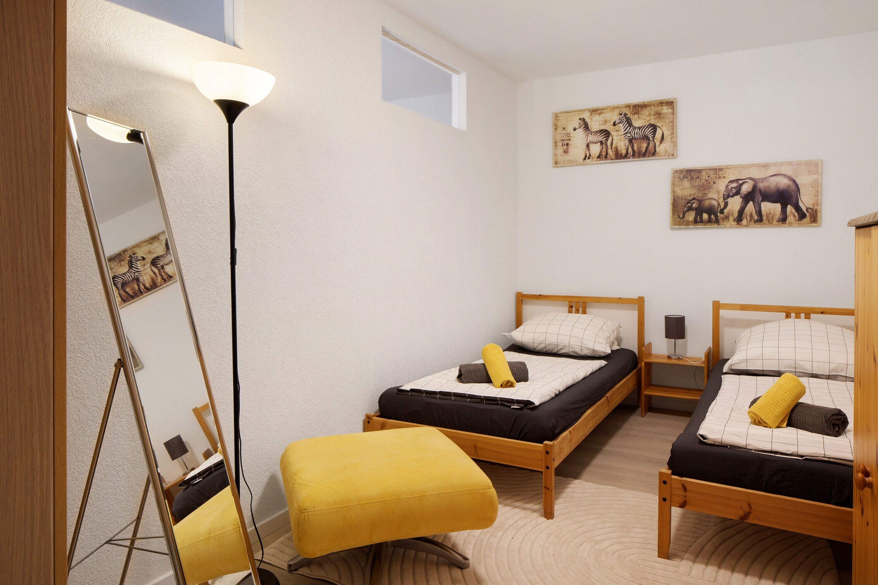 Une chambre à coucher avec deux lits en bois, une lampe sur pied et des œuvres d’art accrochées au mur.
