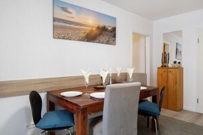Un comedor con una mesa de madera dispuesta para cuatro, un cuadro de una escena de playa y un aparador de madera.