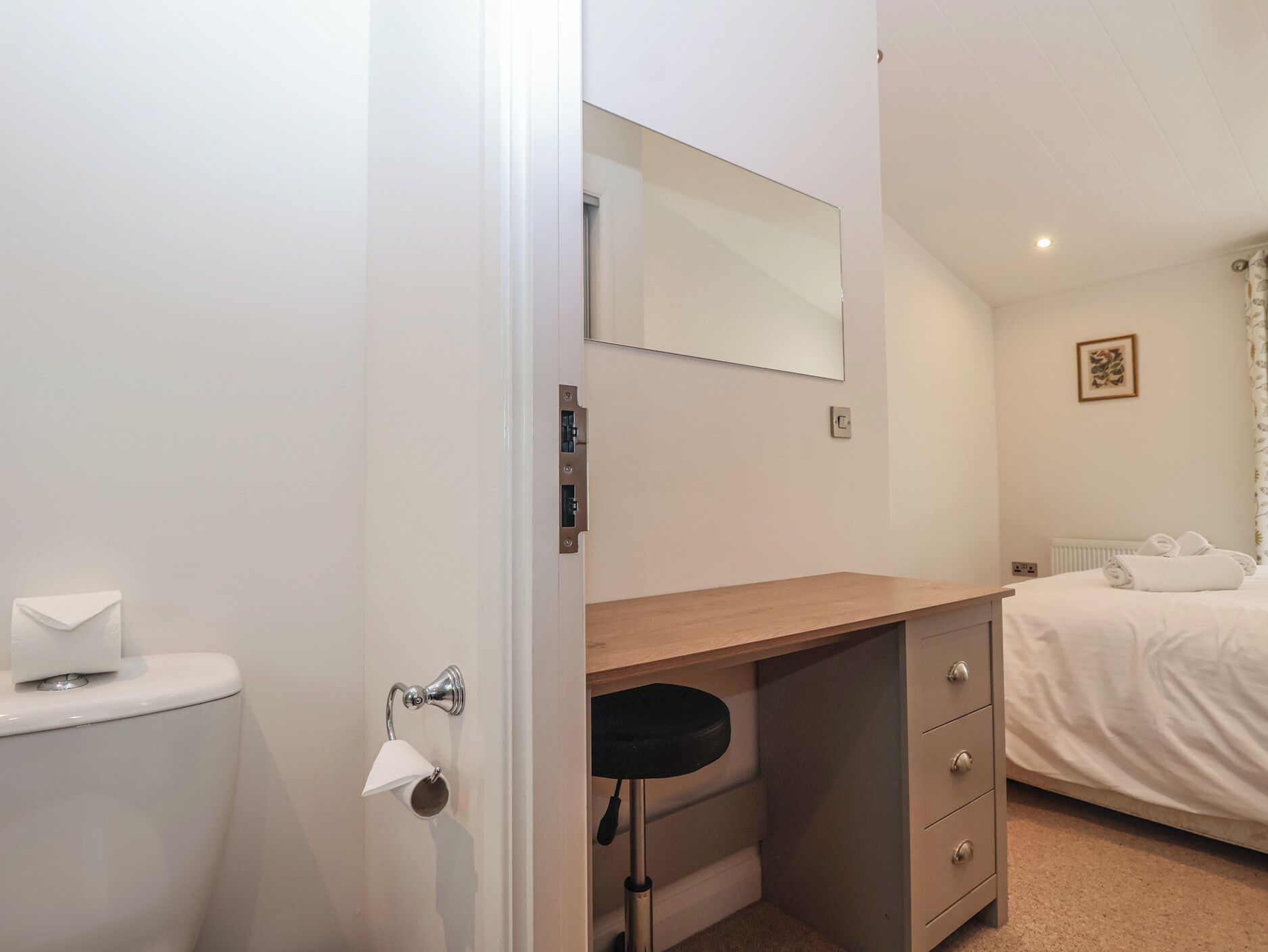 A hotel room with a wooden desk, a mirror, a toilet, a bed, and a radiator.