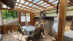 Un patio cubierto con una mesa, sillas y un dardo, además de un muro de piedra.