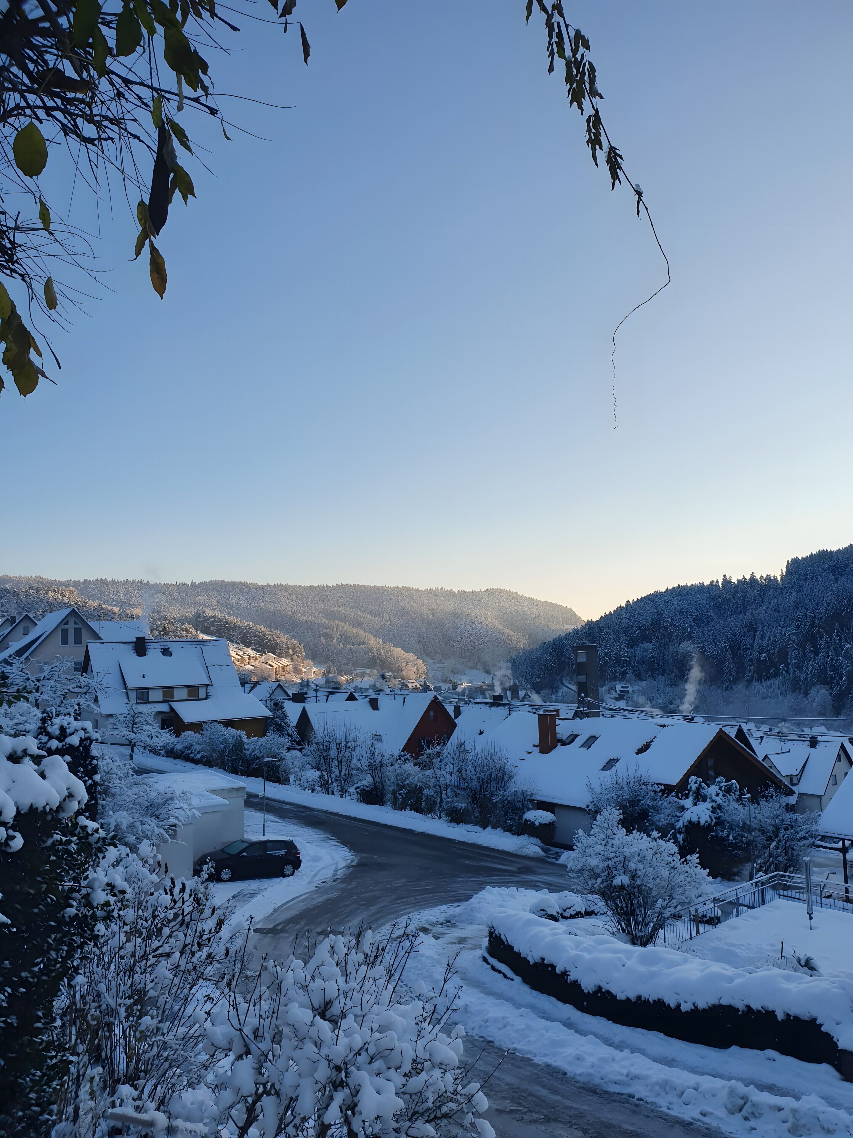 Un village enneigé, avec des maisons traditionnelles, un ciel dégagé et une montagne en arrière-plan.