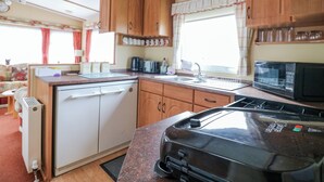 A compact kitchen with wooden cabinets, a microwave, a toaster, and a sink. - 120 Caravan (Great Yarmouth)