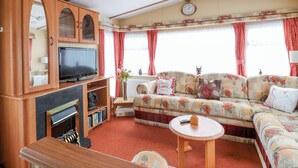 A cozy living room with a sofa, television, wooden cabinets, and a fireplace. - 120 Caravan (Great Yarmouth)